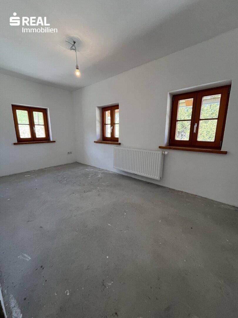 Unfertiger Raum mit Betonboden und weißen Wänden, bereit für den weiteren Ausbau.