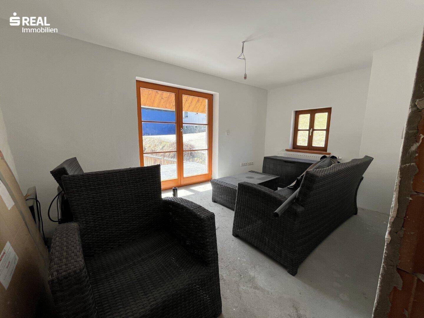 Unfertiger Raum mit Terrassenzugang und Outdoor-Möbeln, wartet auf Fertigstellung.