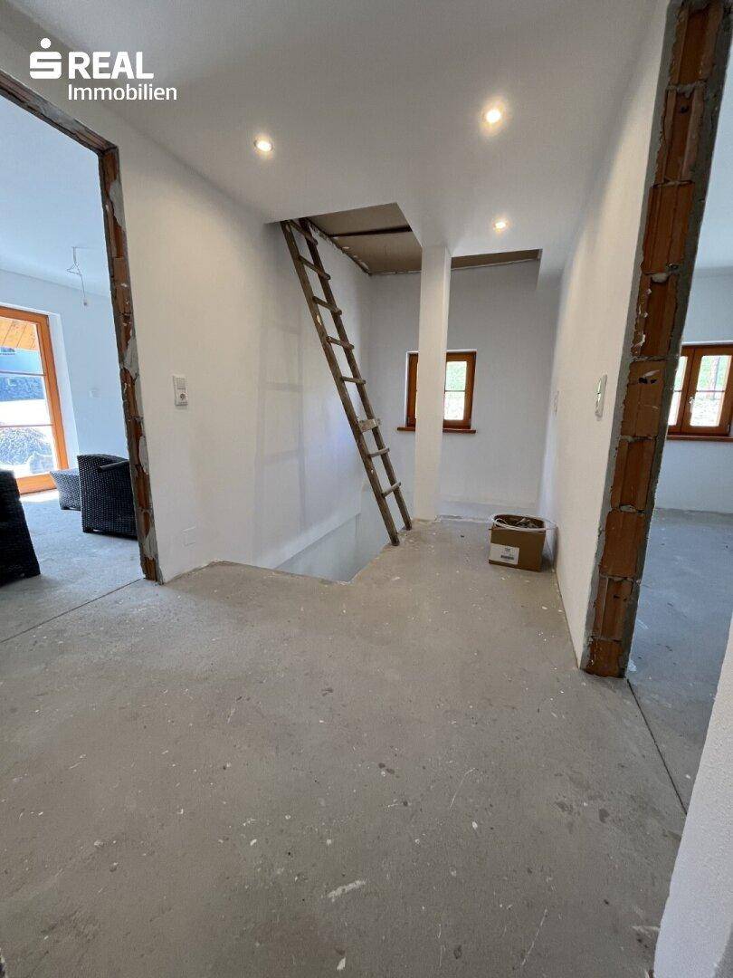 Flur im Rohbau mit Betonboden und Zugang zu weiteren Räumen, bereit für den Ausbau.