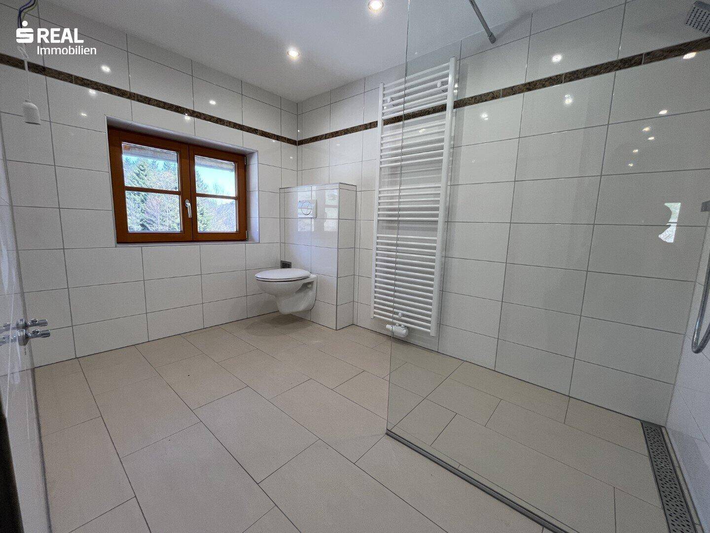 Modernes Badezimmer mit ebenerdiger Dusche, Wand-WC und großen hellen Fliesen.