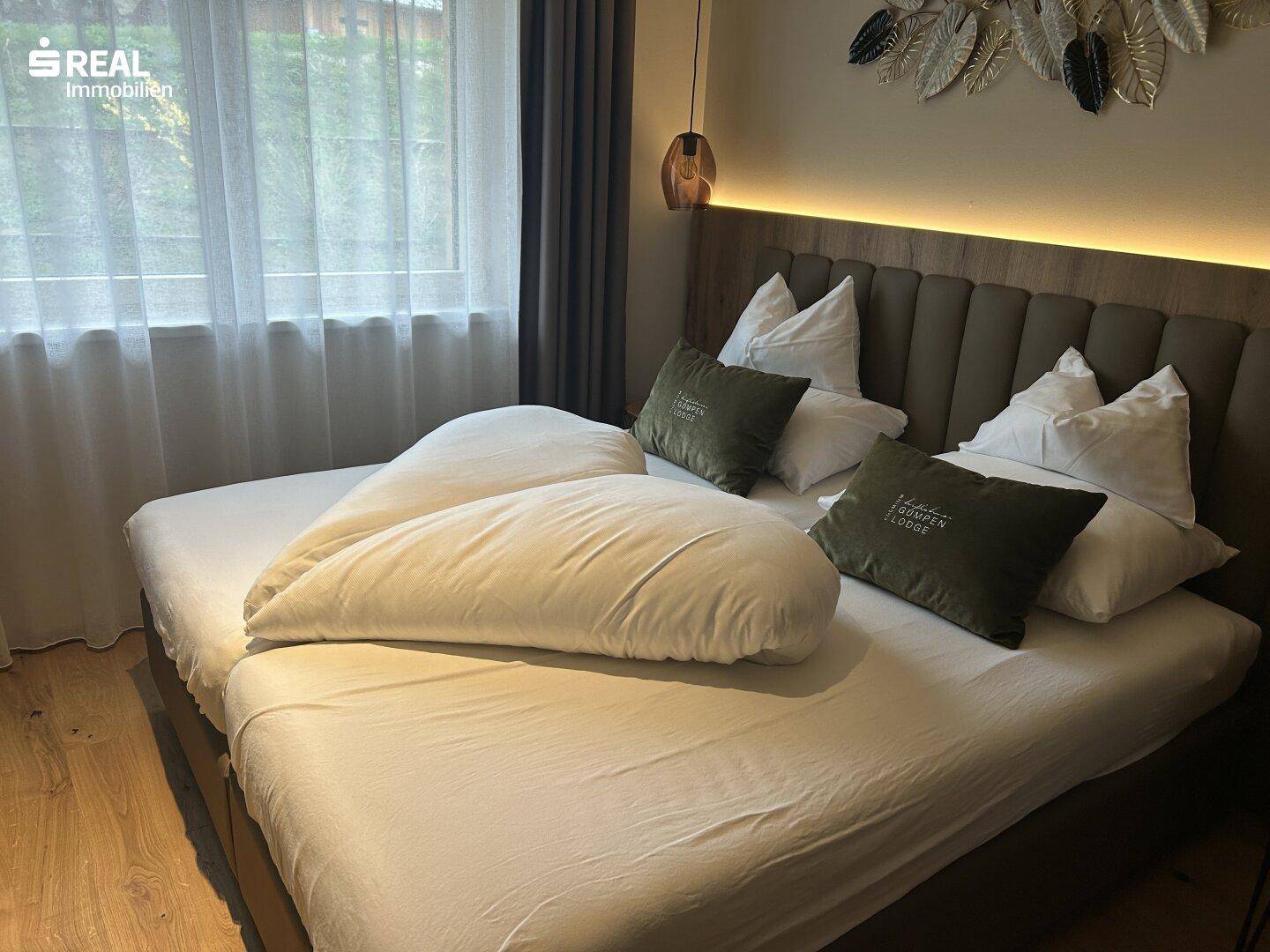 Komfortables Schlafzimmer mit Doppelbett, Holzboden und indirekter Beleuchtung über dem Kopfteil.