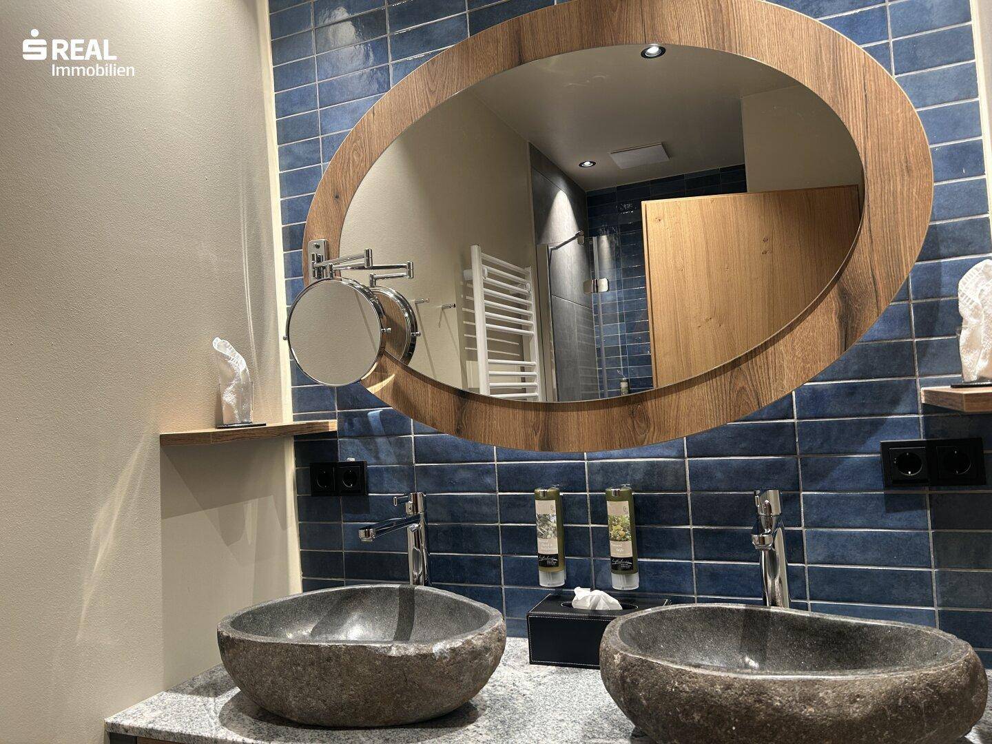 Modernes Badezimmer mit zwei Steinwaschbecken, Holzspiegel und blauen Fliesen.