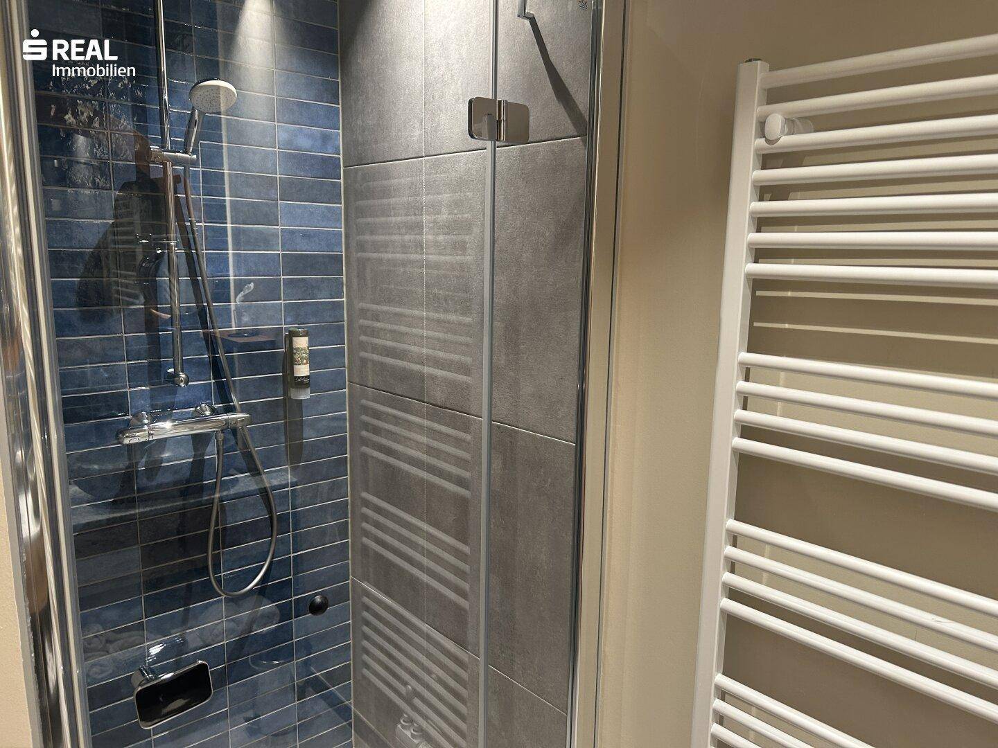 Duschbereich im modernen Badezimmer mit blauen Fliesen und Handtuchheizkörper.