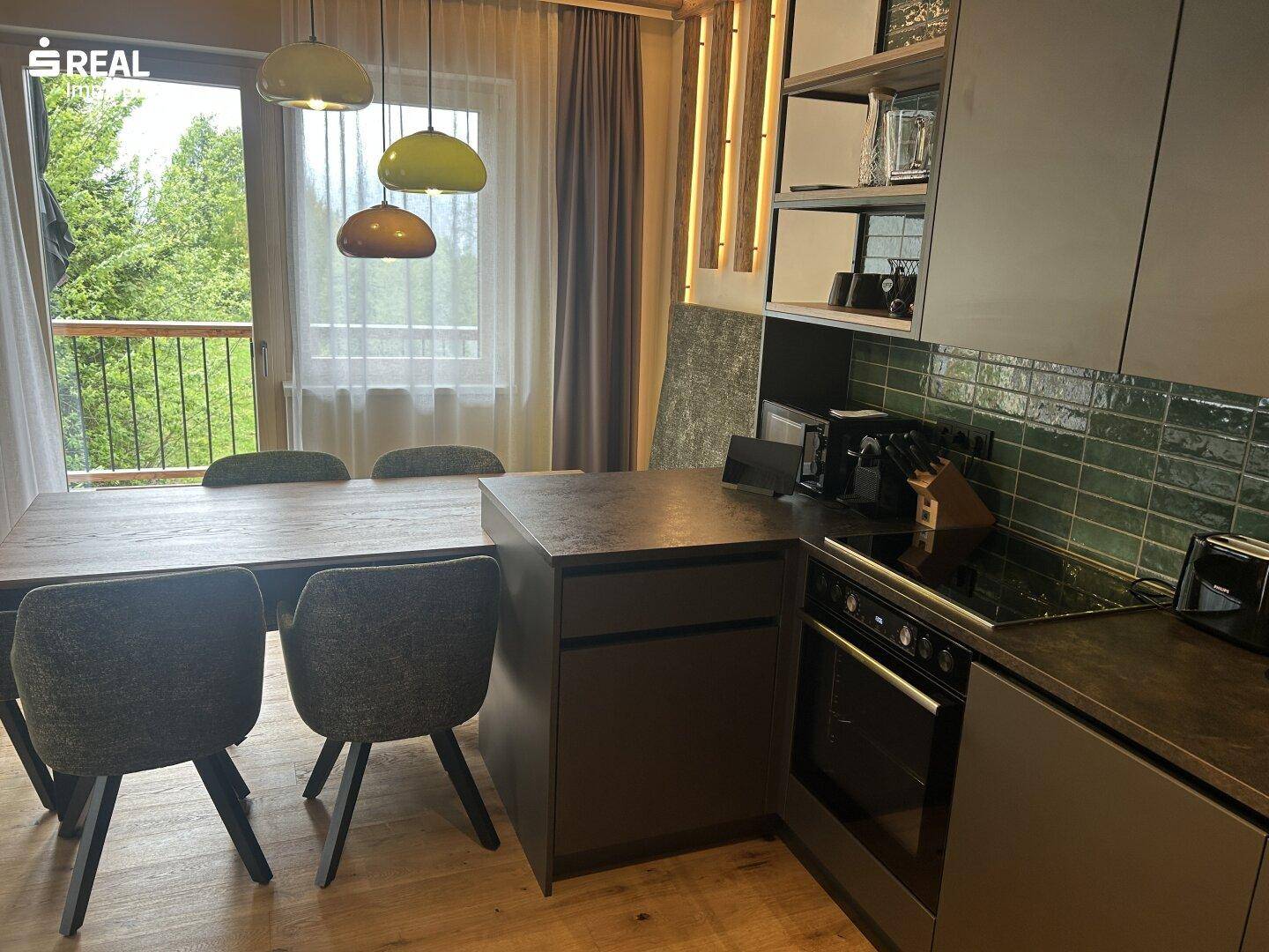 Helle Küche mit Esstisch, dunklen Schränken und Zugang zu einem Balkon.