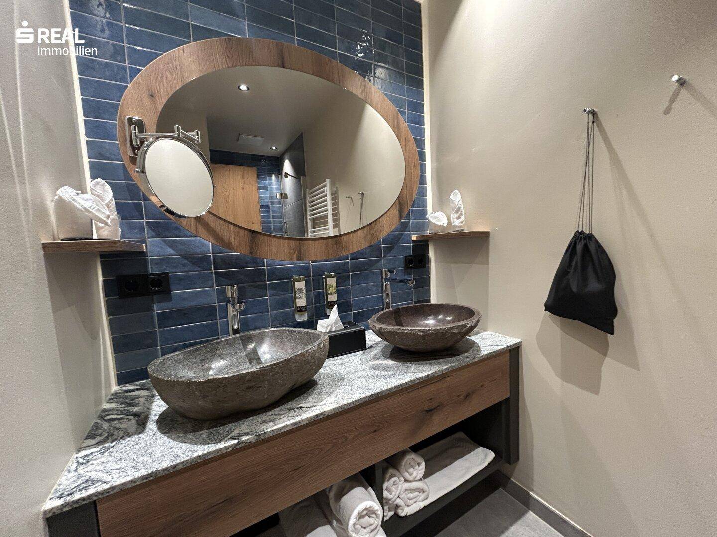 Modernes Badezimmer mit zwei Steinschalenbecken, großem Spiegel und blauen Fliesen an der Wand.