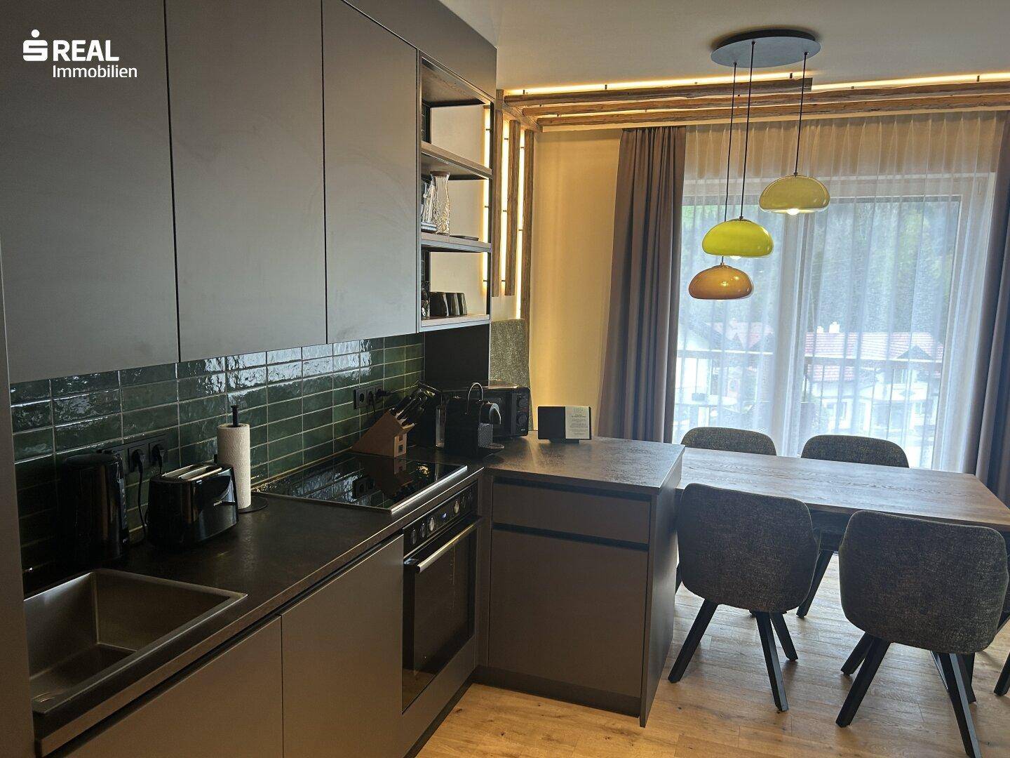 Moderne Küche mit dunklen Schränken, integriertem Kochfeld und Essbereich am Fenster.