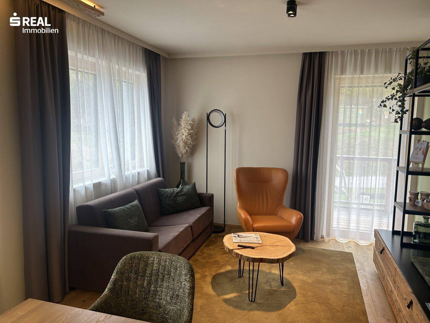 Heller Wohnbereich mit bequemer Couch, Sessel, Holztisch und großen Fenstern für viel Licht.