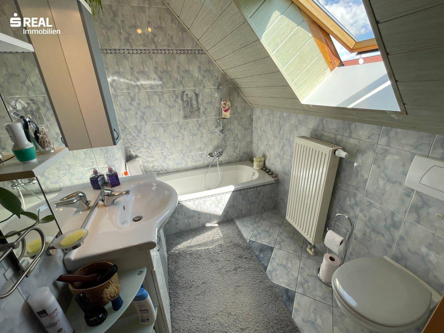 Helles Badezimmer mit Badewanne, WC, Waschbecken und einem Dachfenster für natürliches Licht.