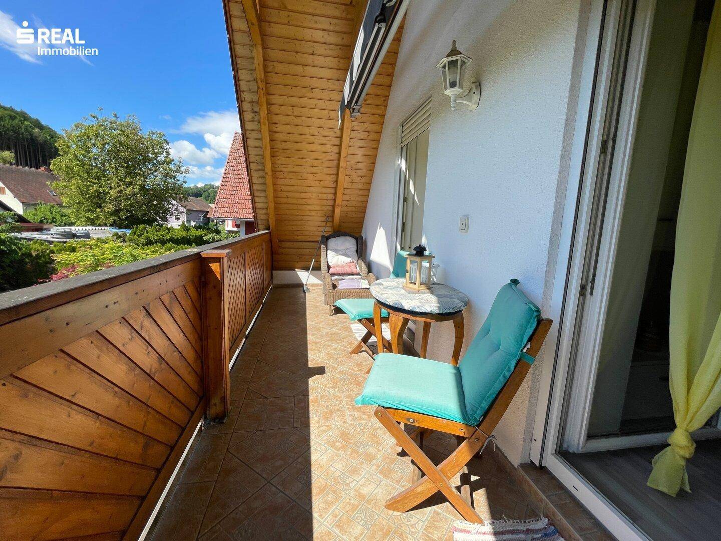 Gemütlicher Balkon mit Holzboden, Sitzgelegenheiten und Blick auf die umliegende Landschaft.
