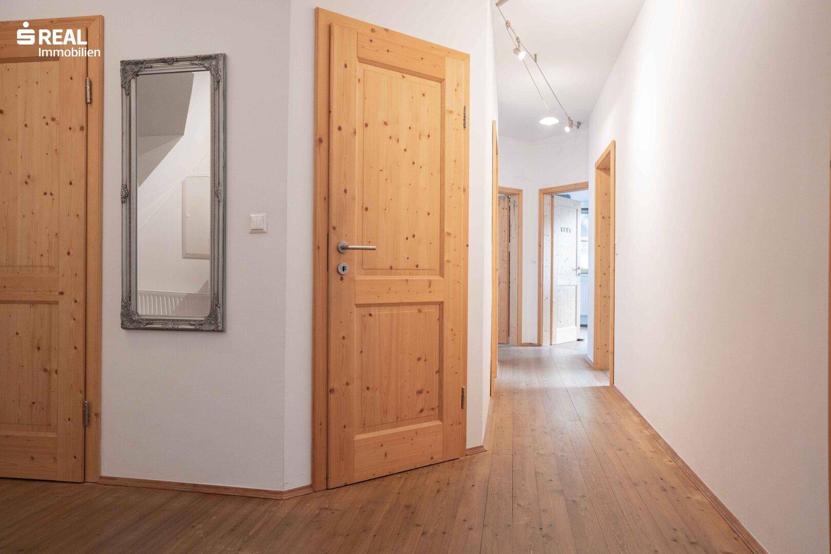 Heller Flur mit Holzboden und Holztüren, der einen Spiegel an der Wand zeigt.