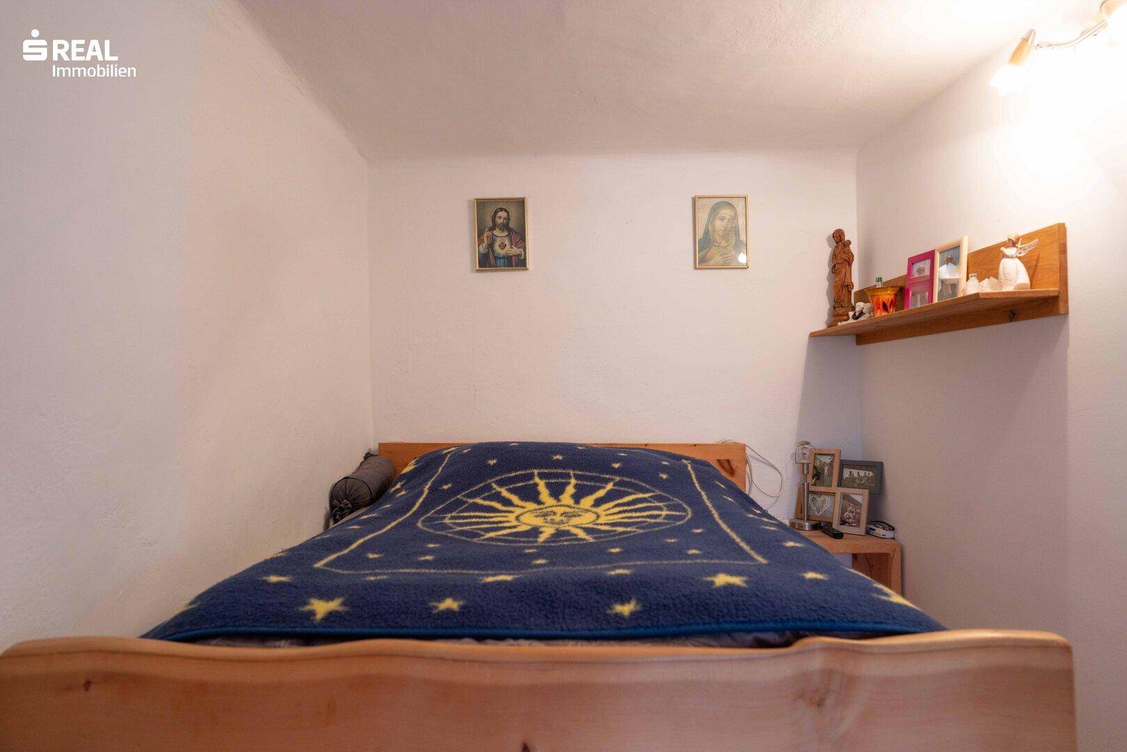 Gemütliches Schlafzimmer mit Holzbett, blauer Decke und religiösen Bildern an der Wand.