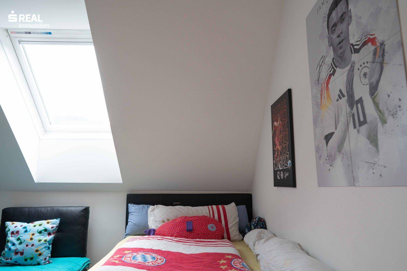 Kinderzimmer im Dachgeschoss mit Einzelbett, Dachfenster und sportlichen Postern an der Wand.