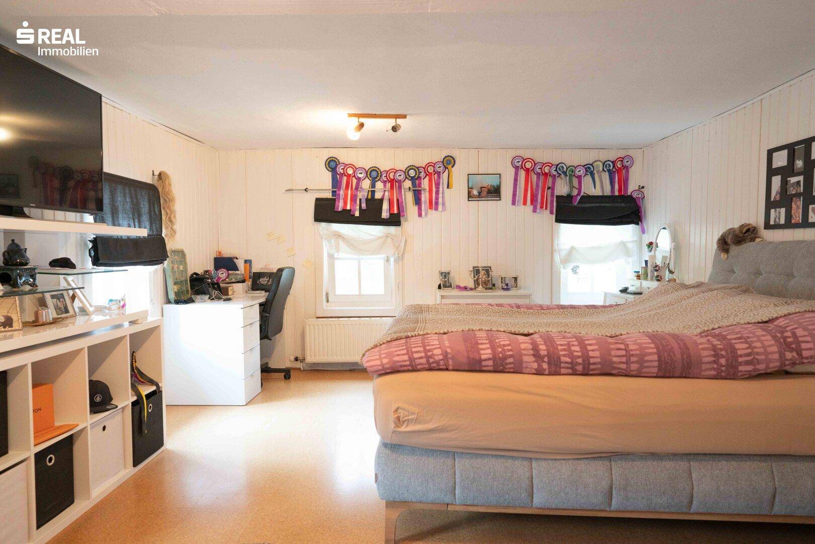 Geräumiges Schlafzimmer mit Doppelbett, Schreibtisch und mehreren Fenstern, hell und wohnlich.