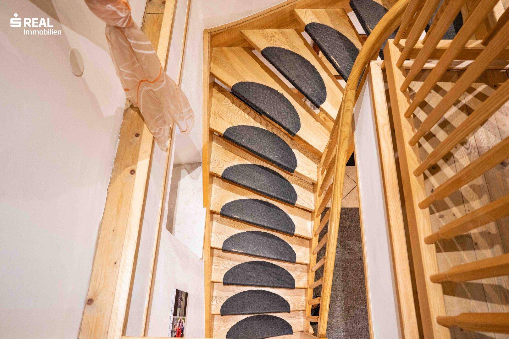 Holztreppe mit Teppichstufen führt in die oberen Etagen, umgeben von hellem Holz.
