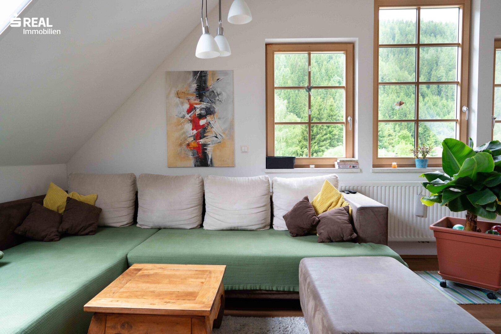 Gemütliche Sitzecke im Dachgeschoss mit großem Sofa, Holztisch und Blick auf die Natur.