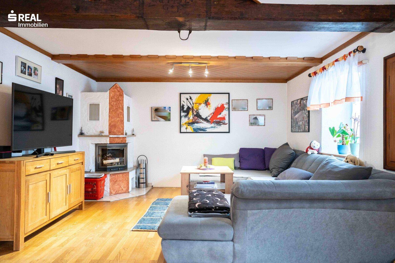 Helles Wohnzimmer mit Holzboden, Kaminofen und gemütlicher Sitzecke unter Holzbalken.