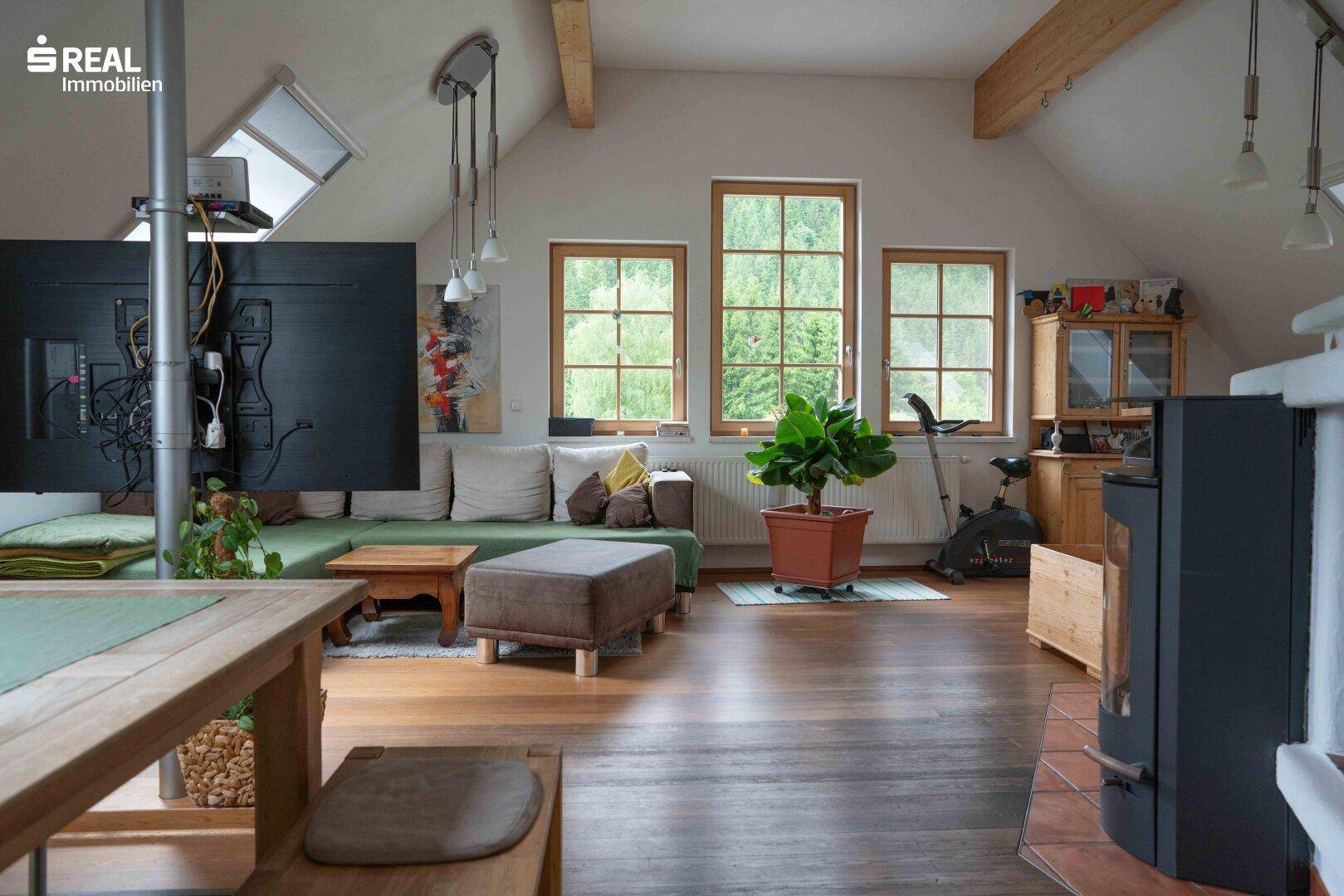 Geräumiges Wohnzimmer im Dachgeschoss mit Holzboden, Kaminofen und Blick ins Grüne.