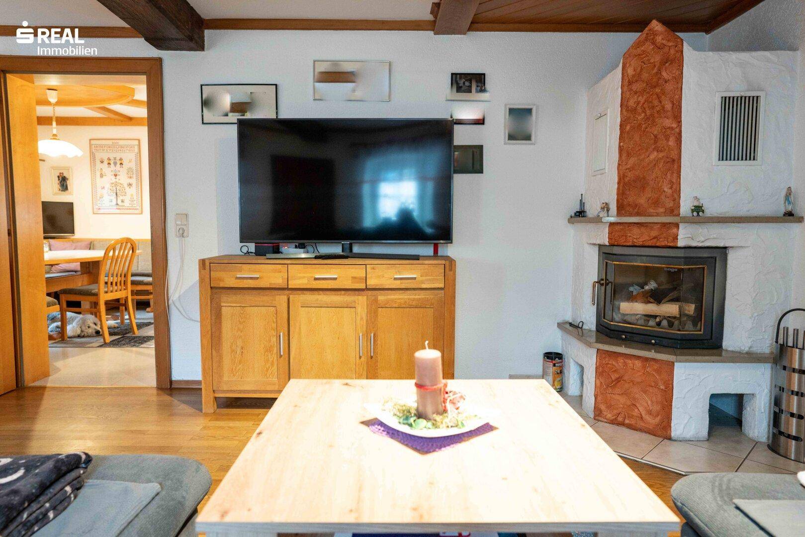 Detailansicht des Wohnzimmers mit Kaminofen, Fernseher und Holztisch in rustikalem Ambiente.