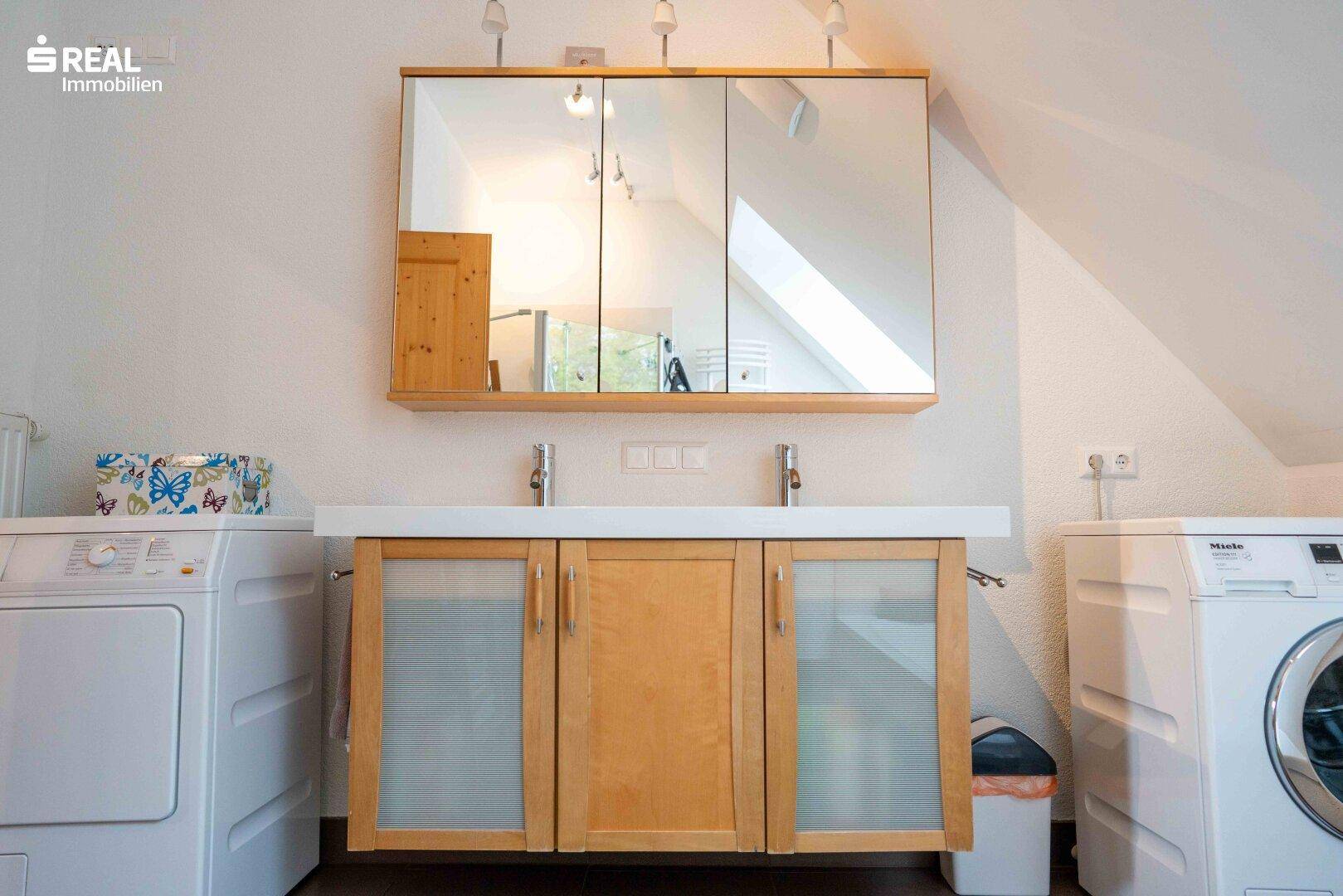 Badezimmer mit Doppelwaschbecken, Spiegelschrank und integrierten Waschmaschinen im Dachgeschoss.