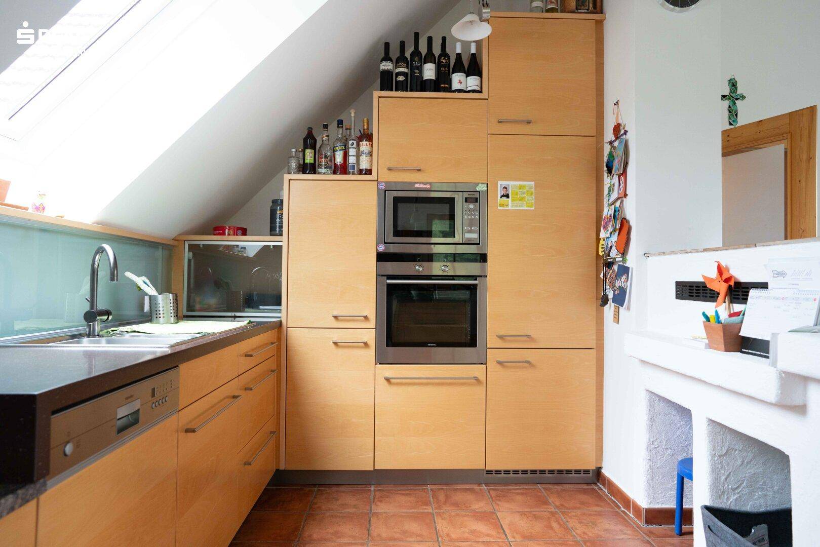 Helle Küche im Dachgeschoss mit Holzeinbauten, modernen Geräten und Terrakotta-Boden.