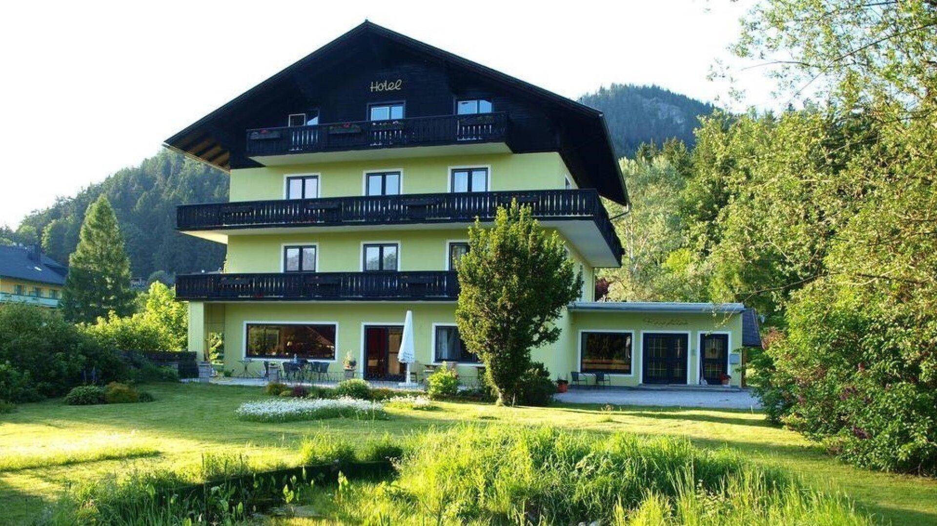 Gepflegter Gartenbereich mit Rasenfläche und Sitzgelegenheiten vor dem traditionellen Gebäude mit Bergblick.