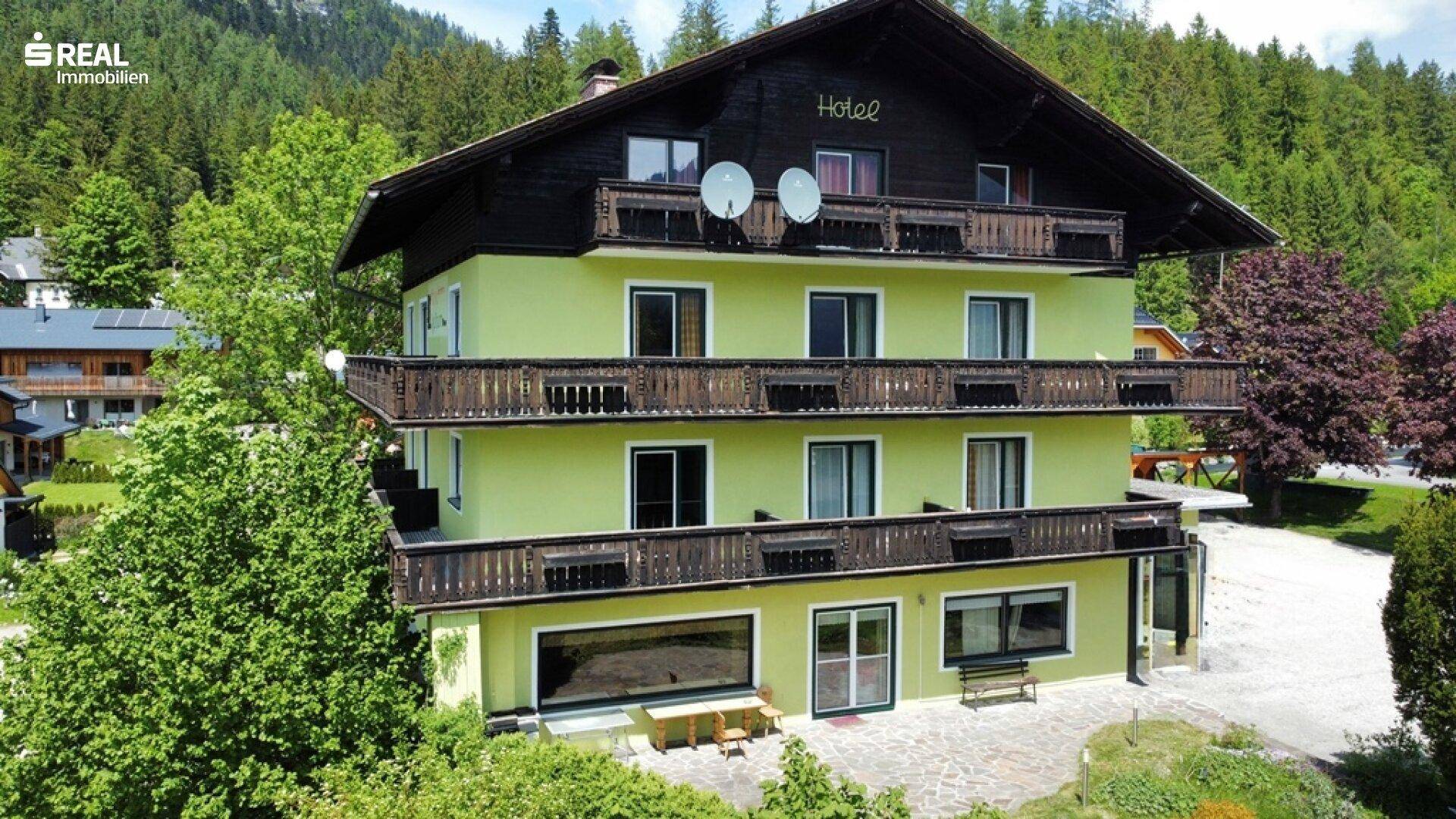 Ansicht des traditionellen Gebäudes mit grüner Fassade, Holzbalkonen und umgebender Naturlandschaft.