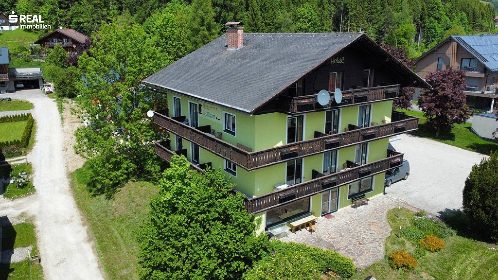 Luftaufnahme des Gebäudes mit grüner Fassade, umgeben von Bäumen und einer ländlichen Umgebung.