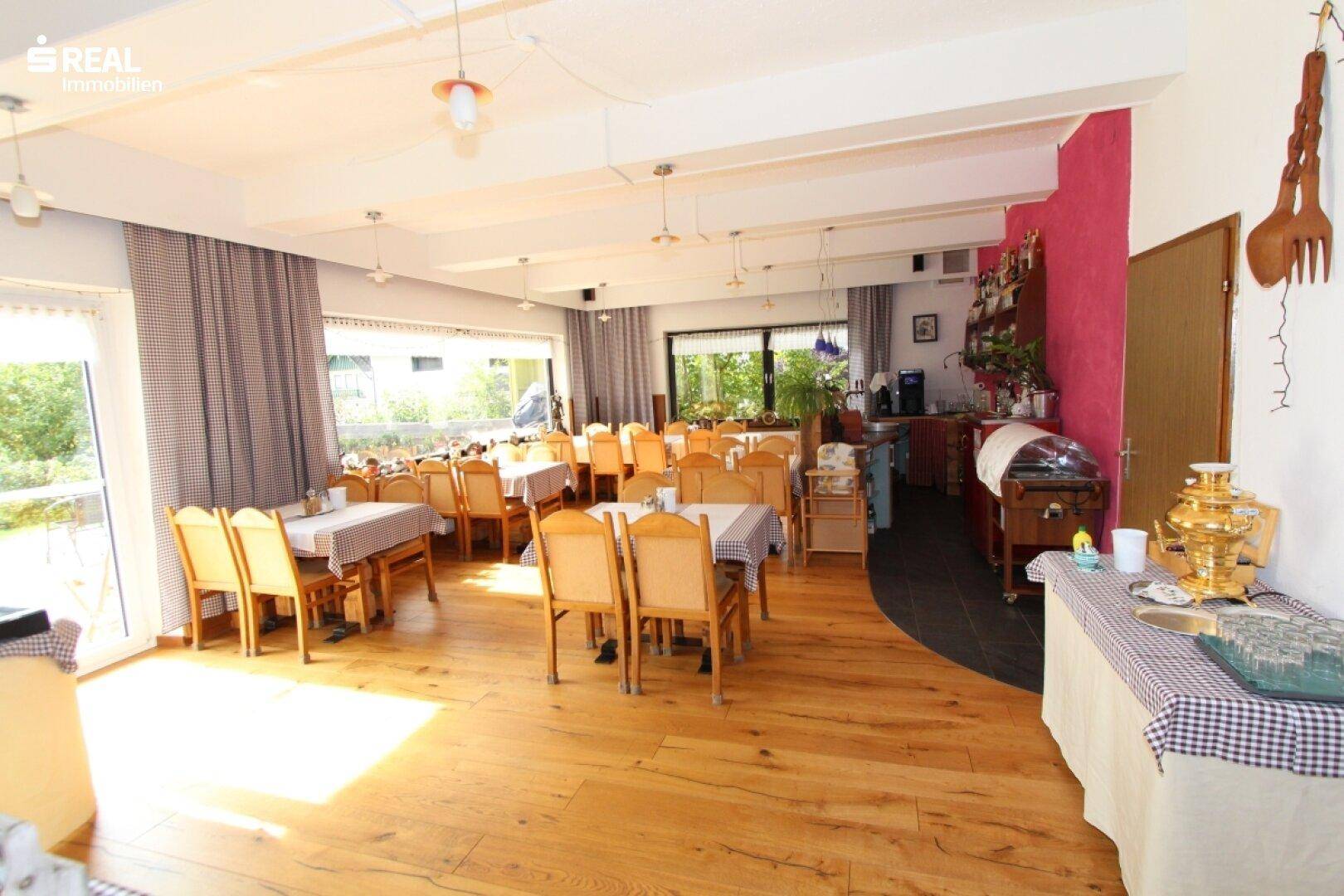 Heller Speisesaal mit Holzboden, Buffetbereich und Blick ins Grüne durch große Fenster.
