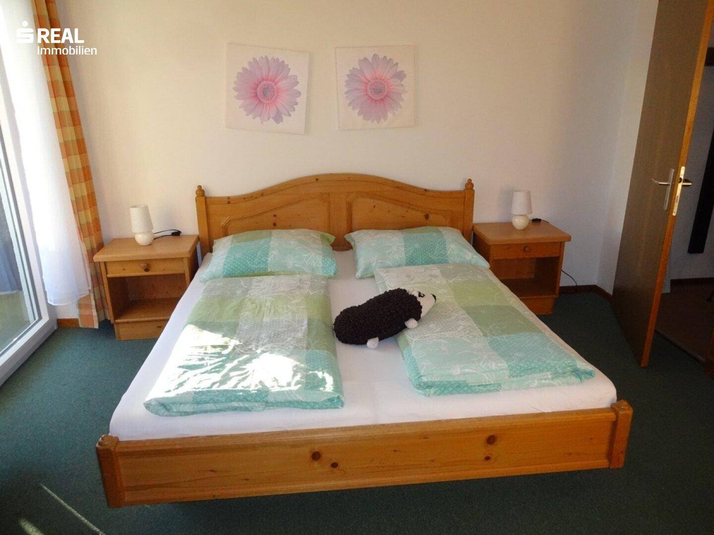 Helles Schlafzimmer mit Holzdoppelbett, grünem Teppichboden und Zugang zum Balkon.
