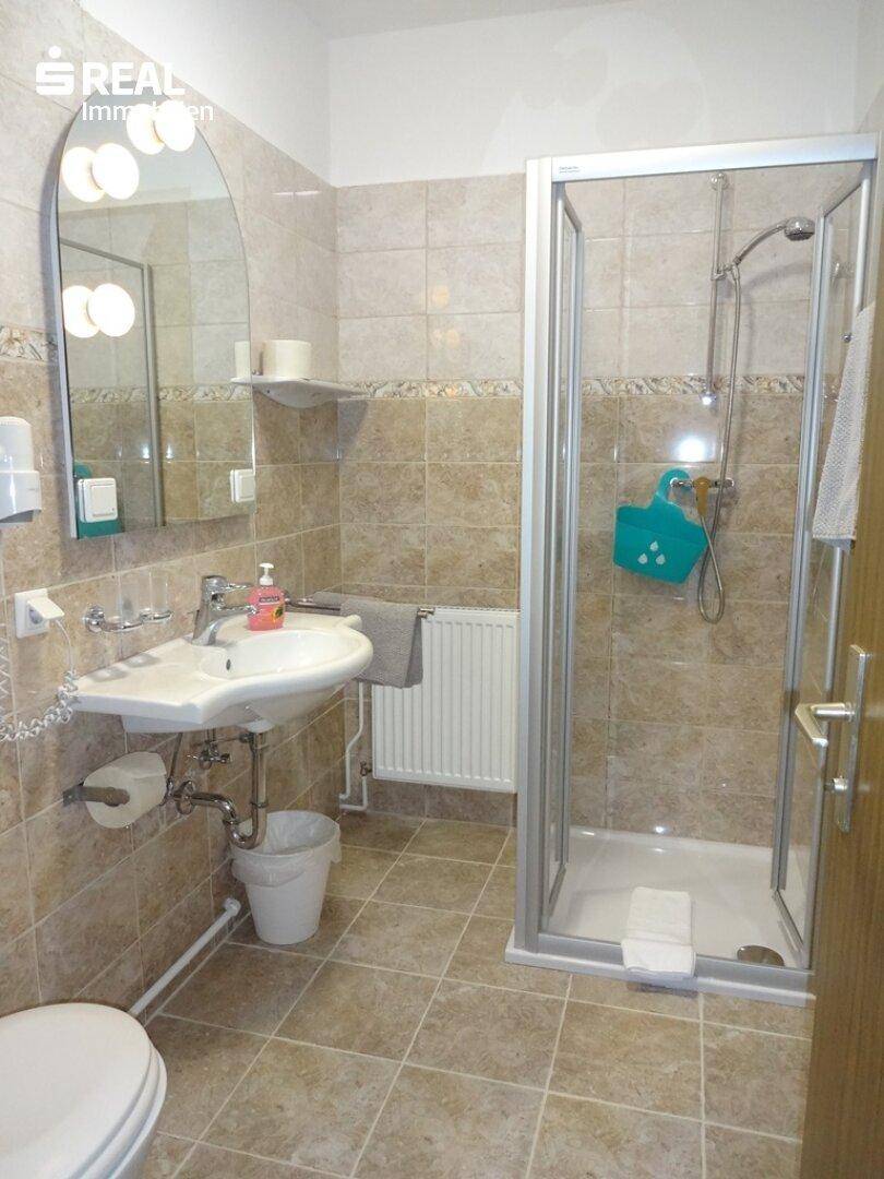 Gefliestes Badezimmer mit Duschkabine, Einzelwaschbecken und Heizkörper.