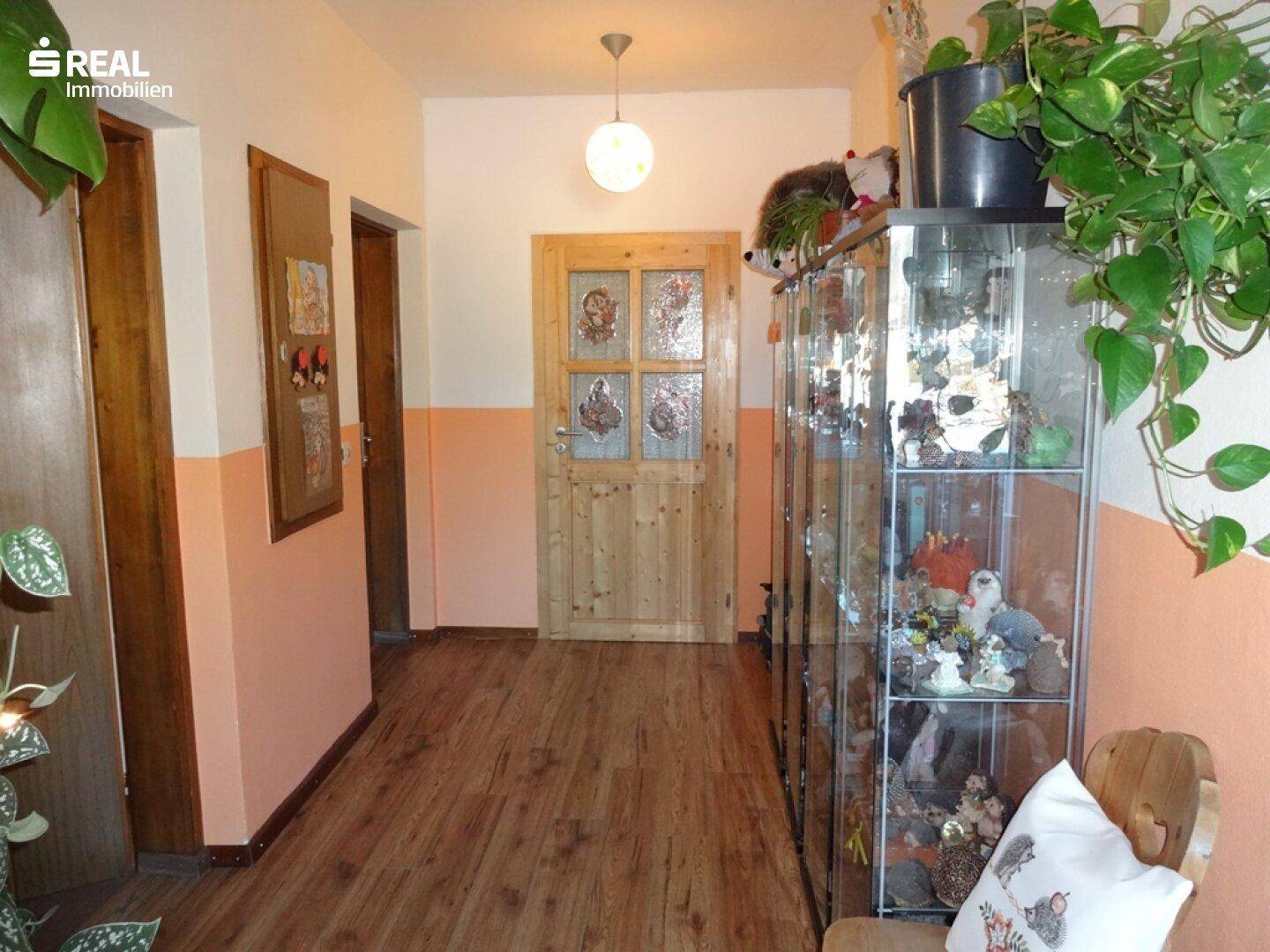 Heller Flur mit Holzboden, zweifarbigen Wänden und einer Vitrine.