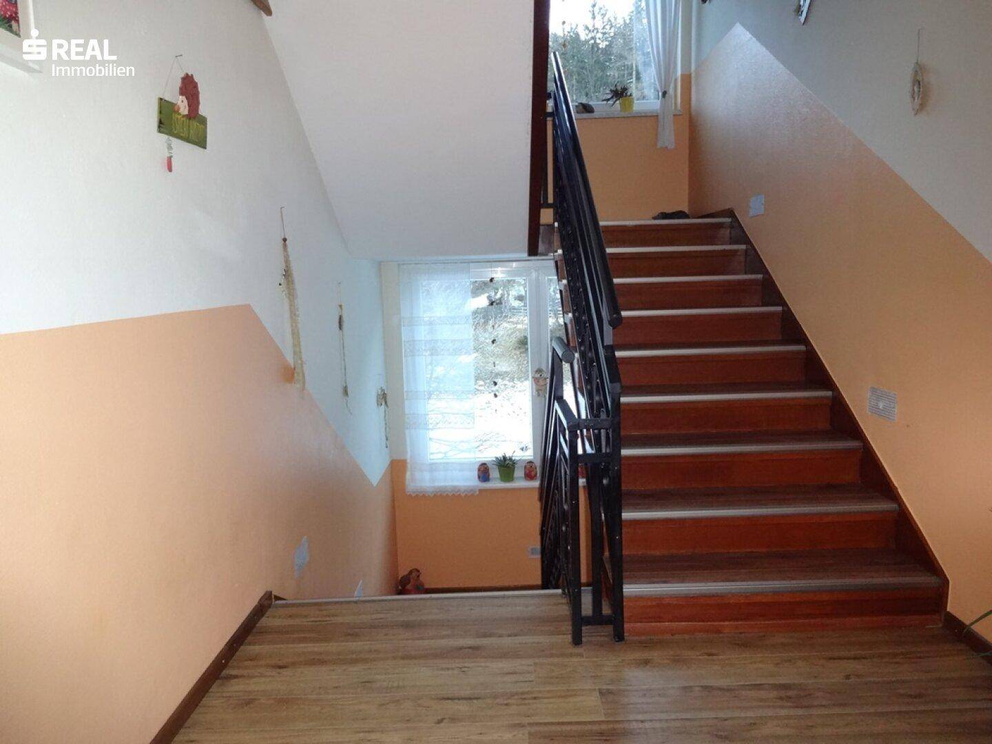 Holztreppe mit Metallgeländer in einem hellen Treppenhaus.