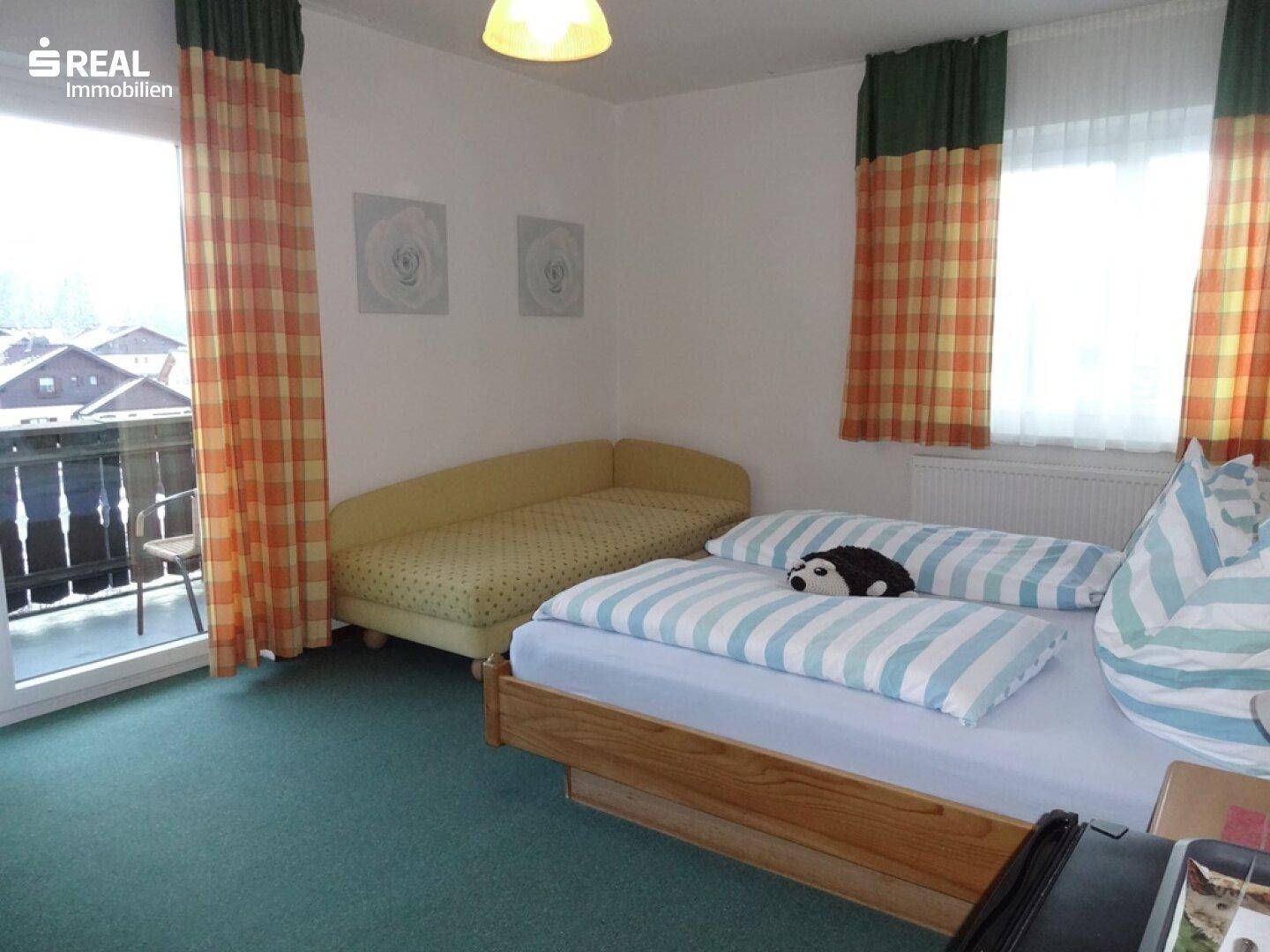 Gemütliches Schlafzimmer mit Doppelbett, grünem Teppich und Balkonzugang.