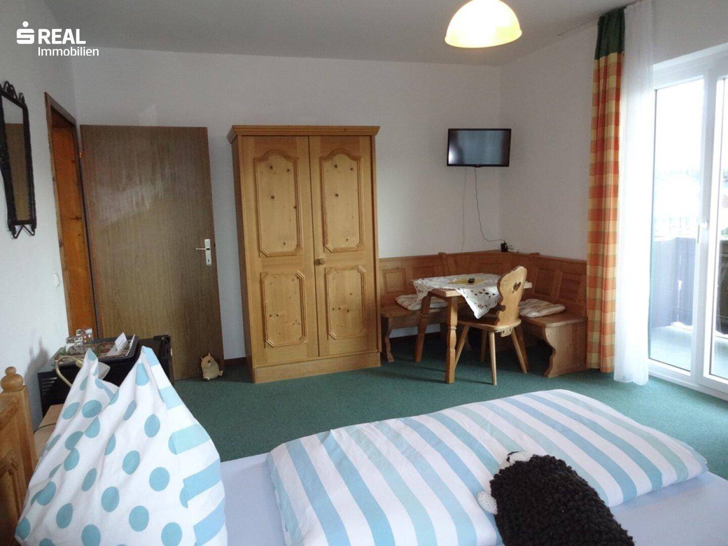 Schlafzimmer mit Doppelbett, Holzschrank, kleiner Sitzecke und Balkonzugang.