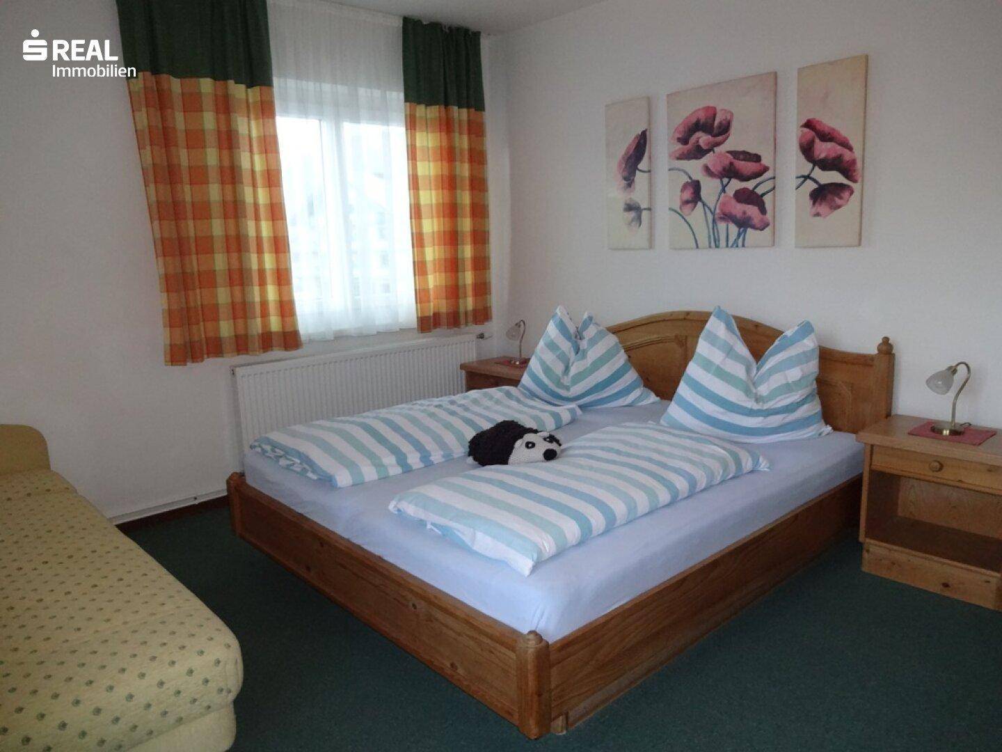 Helles Schlafzimmer mit Doppelbett, grünem Teppichboden und floraler Wanddekoration.