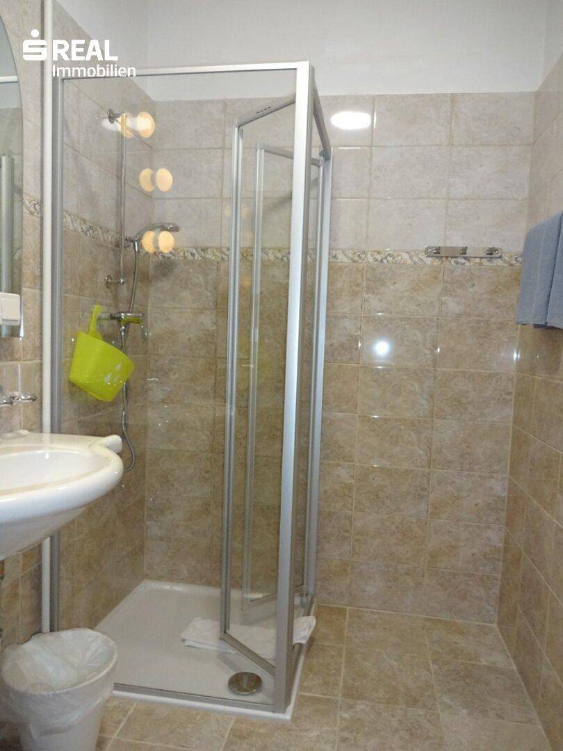 Gefliestes Badezimmer mit Duschkabine, Einzelwaschbecken und hellen Fliesen.