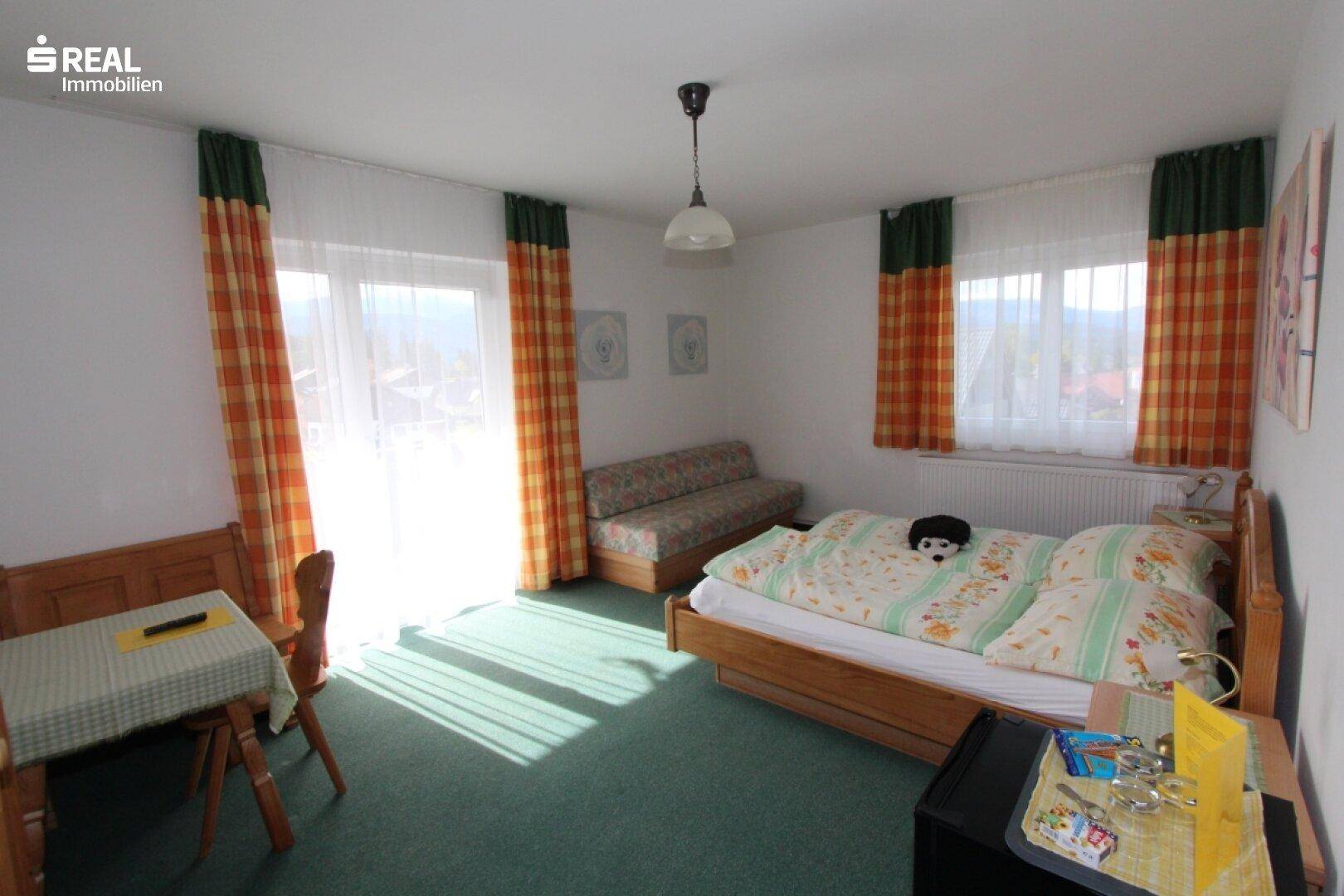 Helles Schlafzimmer mit Doppelbett, grünem Teppich und kleiner Sitzecke.
