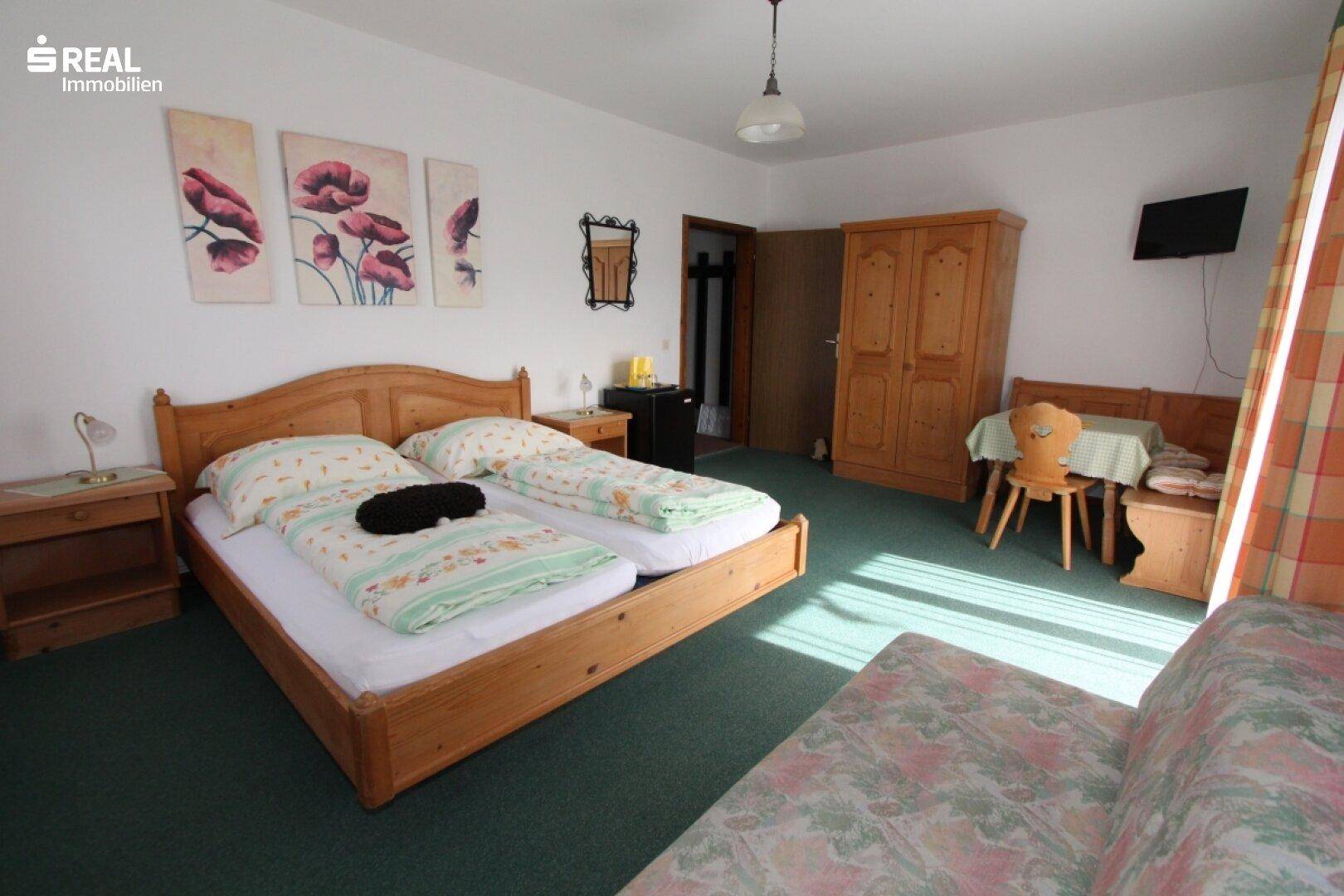 Geräumiges Schlafzimmer mit Doppelbett, grünem Teppich und floralen Bildern an der Wand.