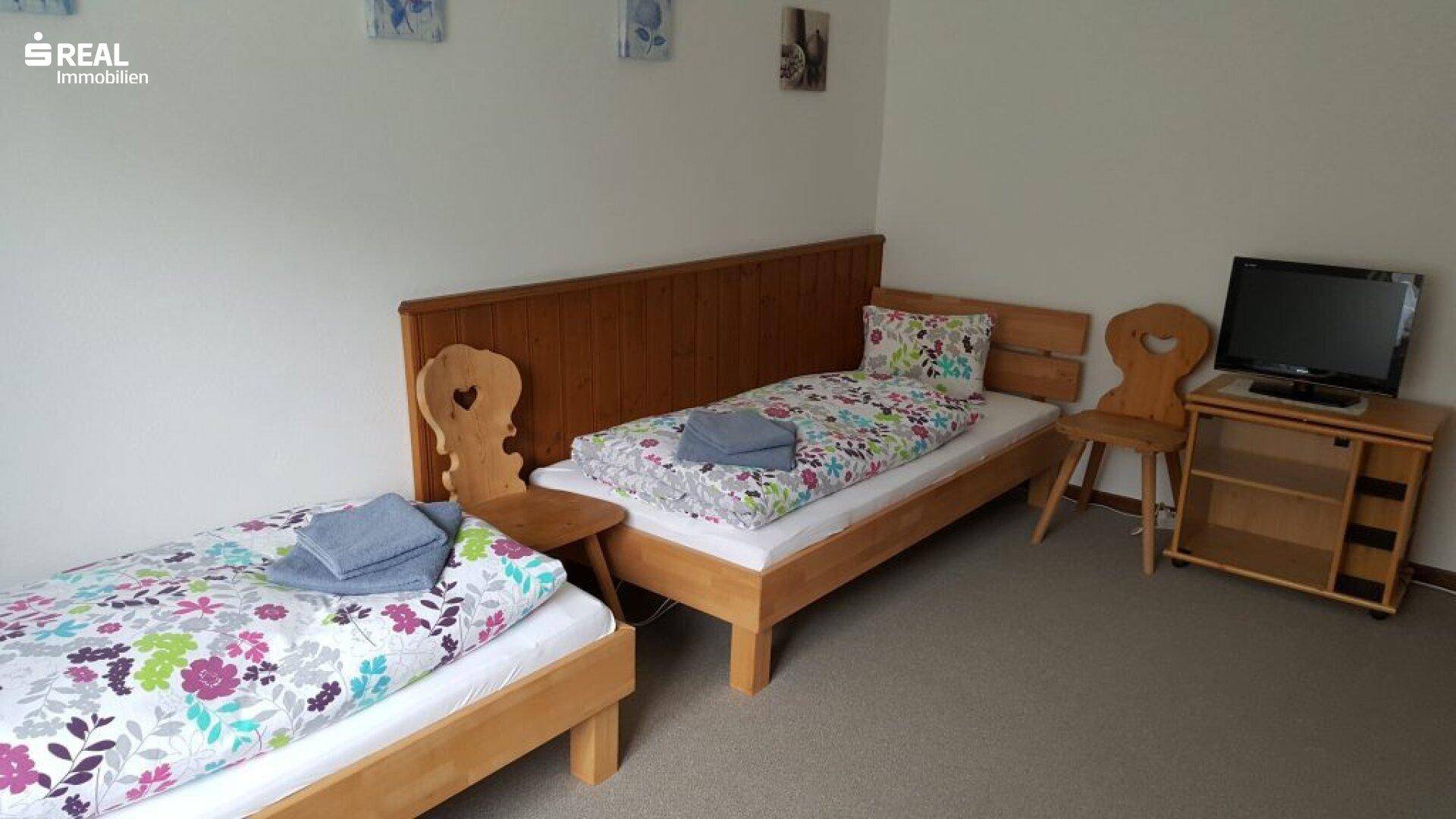 Helles Schlafzimmer mit zwei Einzelbetten, Holzmöbeln und floraler Bettwäsche.