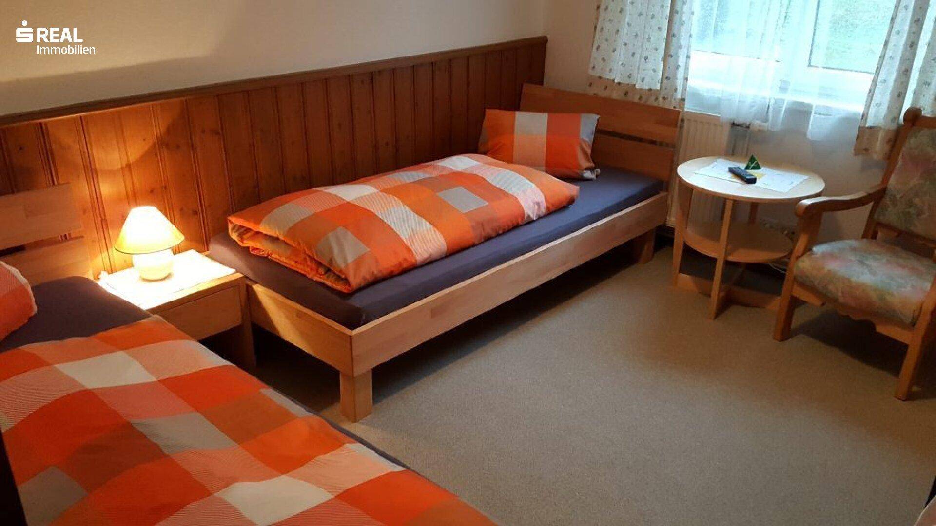 Gemütliches Schlafzimmer mit zwei Einzelbetten, Holzvertäfelung und Fenster mit Vorhängen.