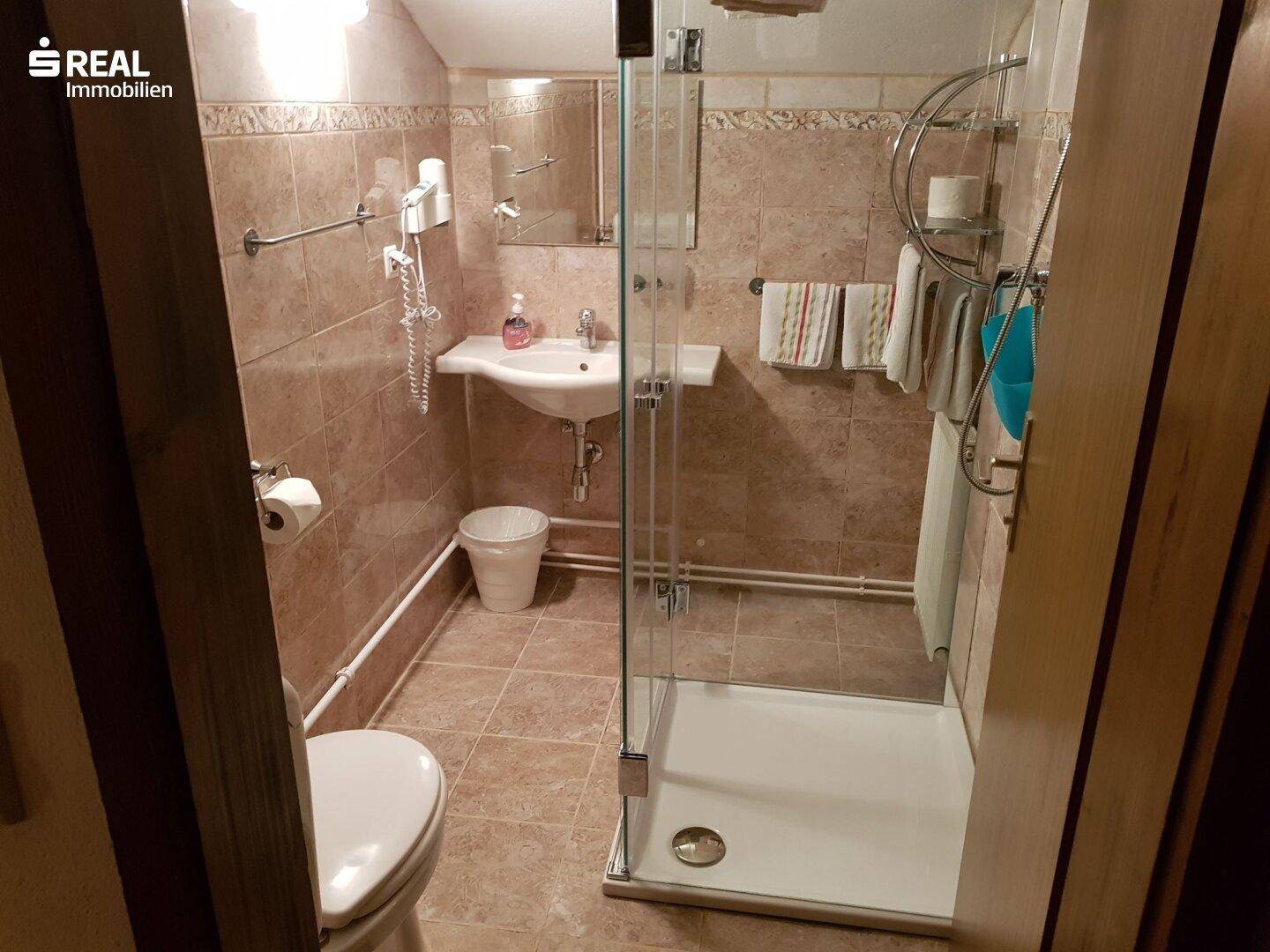 Helles Badezimmer mit beigefarbenen Fliesen, Dusche, WC und Waschbecken.