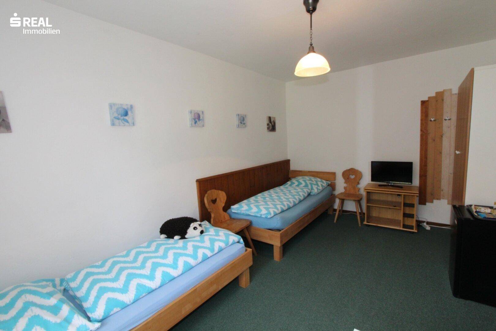 Schlafzimmer mit zwei Einzelbetten, Holzmöbeln und grünem Teppichboden.
