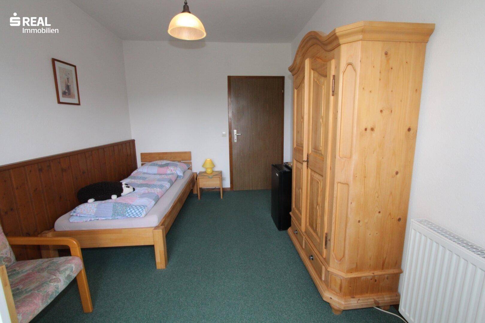 Schlafzimmer mit Einzelbett, großem Holzschrank und Heizkörper an der Wand.