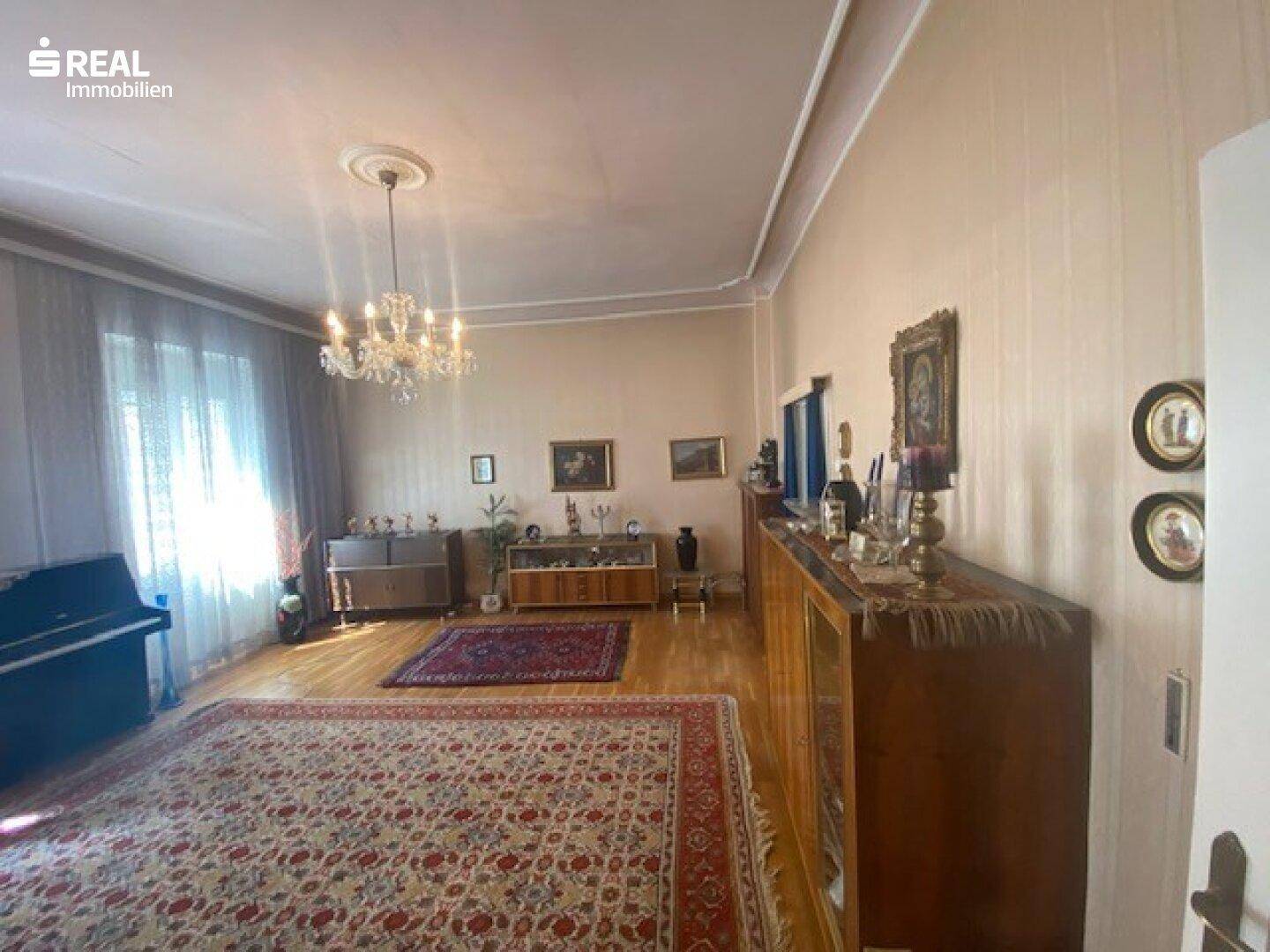 Geräumiges Wohnzimmer mit klassischer Einrichtung, Kronleuchter und Parkettboden.