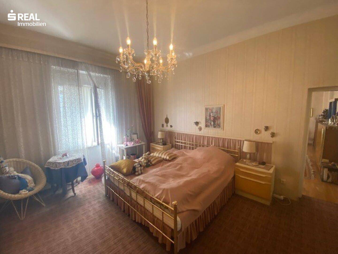 Helles Schlafzimmer mit Doppelbett, Kronleuchter und traditioneller Tapete.