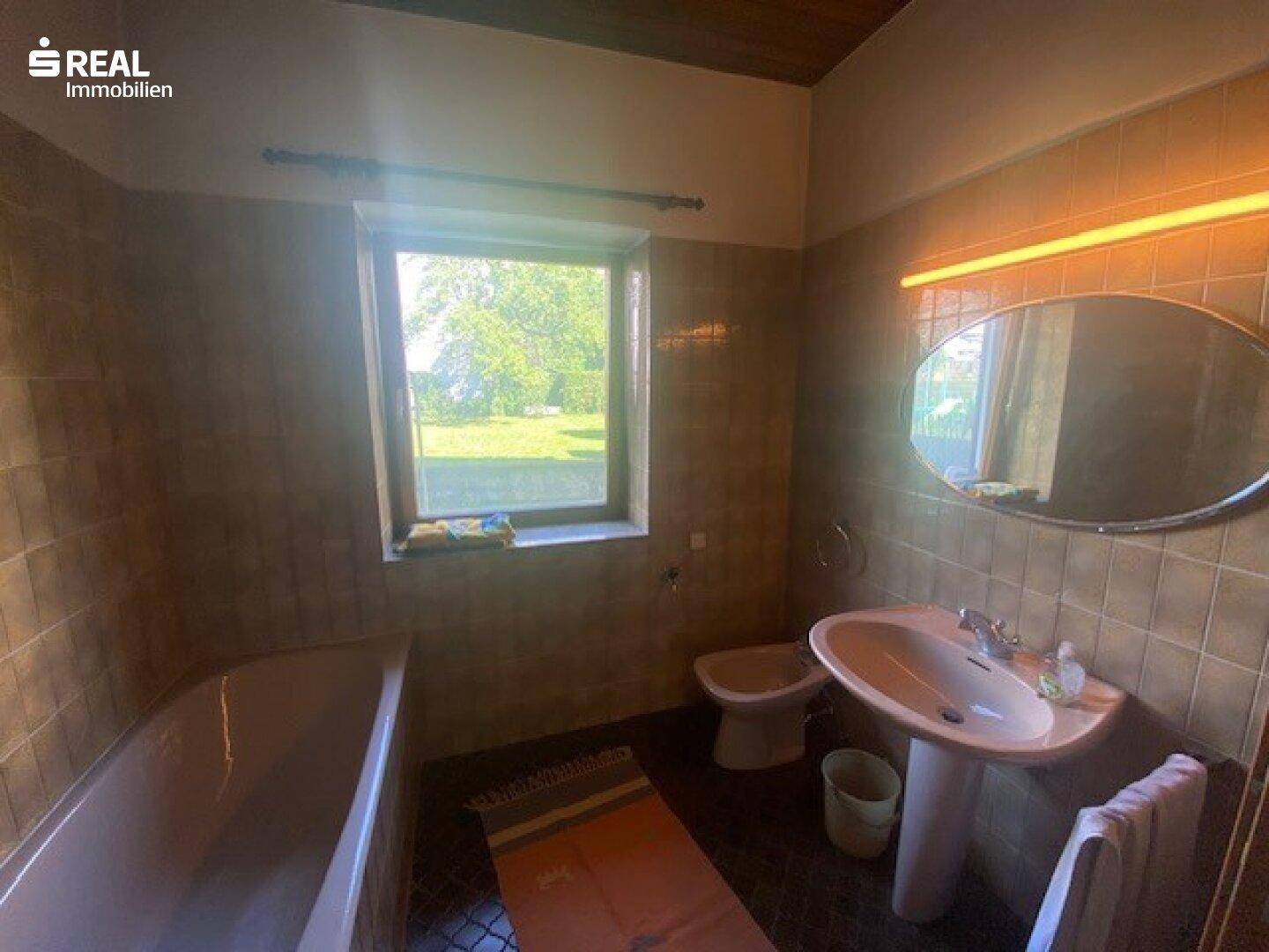 Badezimmer mit Waschbecken, Toilette und Fenster mit Blick ins Grüne.
