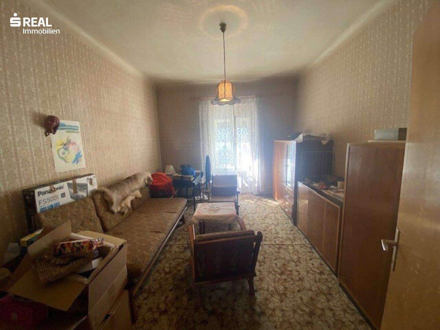 Unklarer Innenraum mit Sofa, Kartons und Fenster, möglicherweise ein Abstellraum.