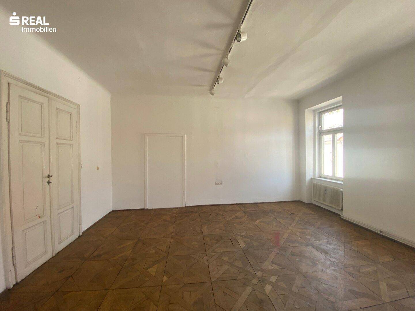 Helles Zimmer mit Fischgrätparkett und weiß gestrichenen Wänden, bereit zur individuellen Gestaltung.