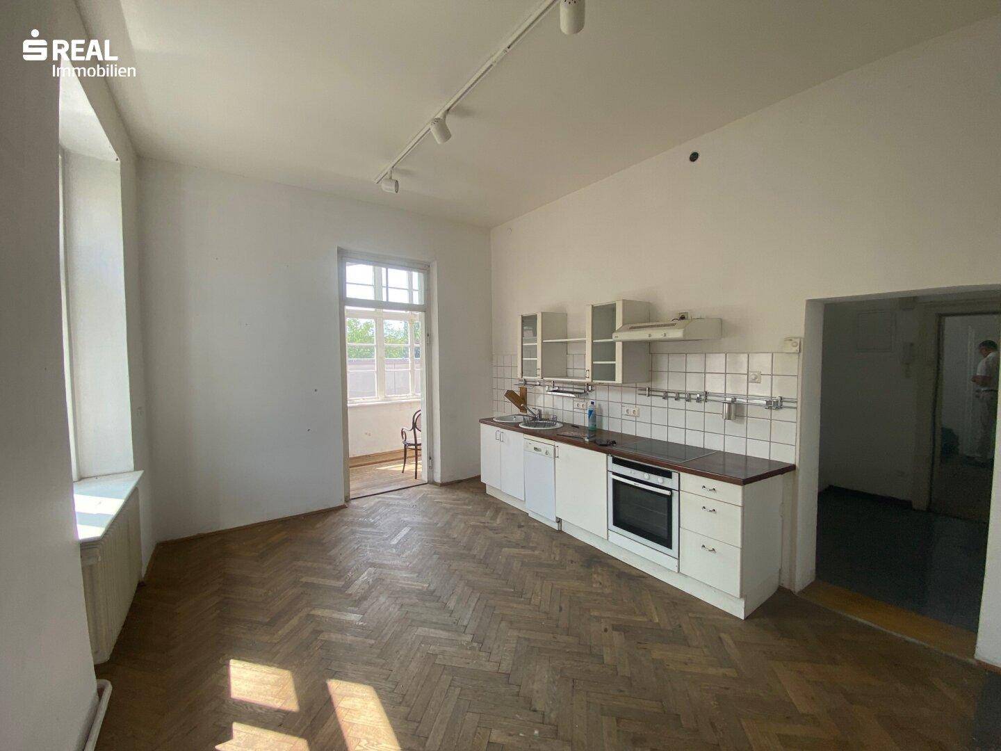 Einfache Küche mit weißer Einbauzeile, Herd und Zugang zu einem kleinen Balkon.
