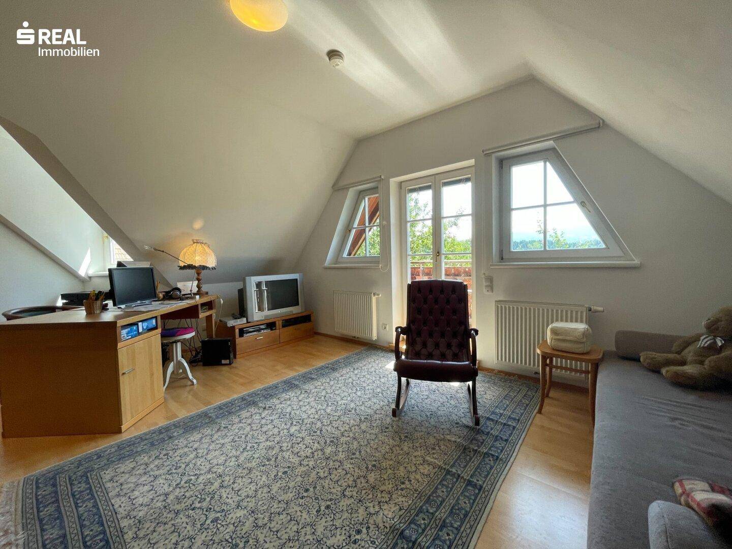 Helles Zimmer im Dachgeschoss mit schrägen Wänden, Holzboden und Blick ins Grüne.